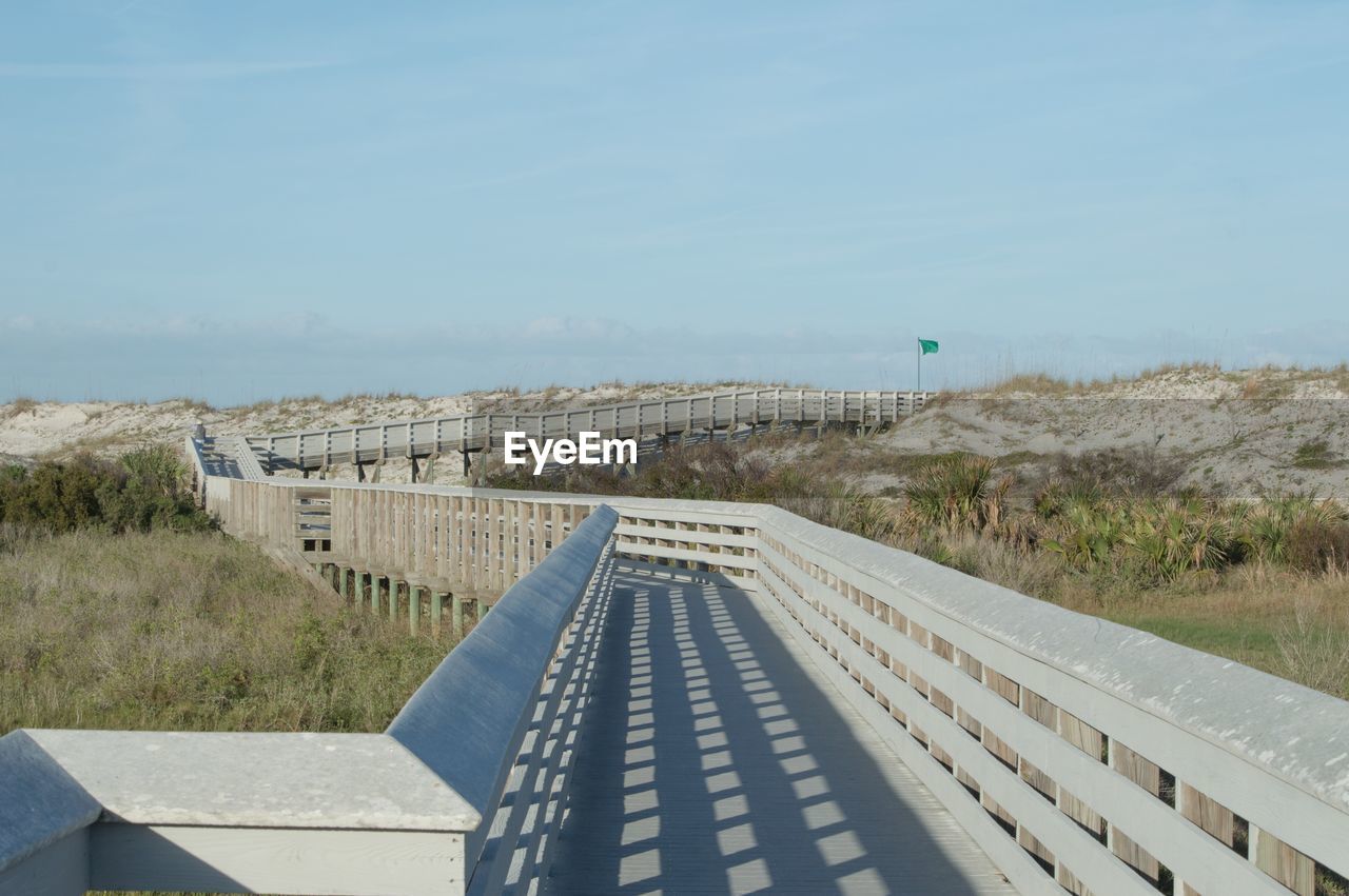 Boardwalk over field against clear blue sky