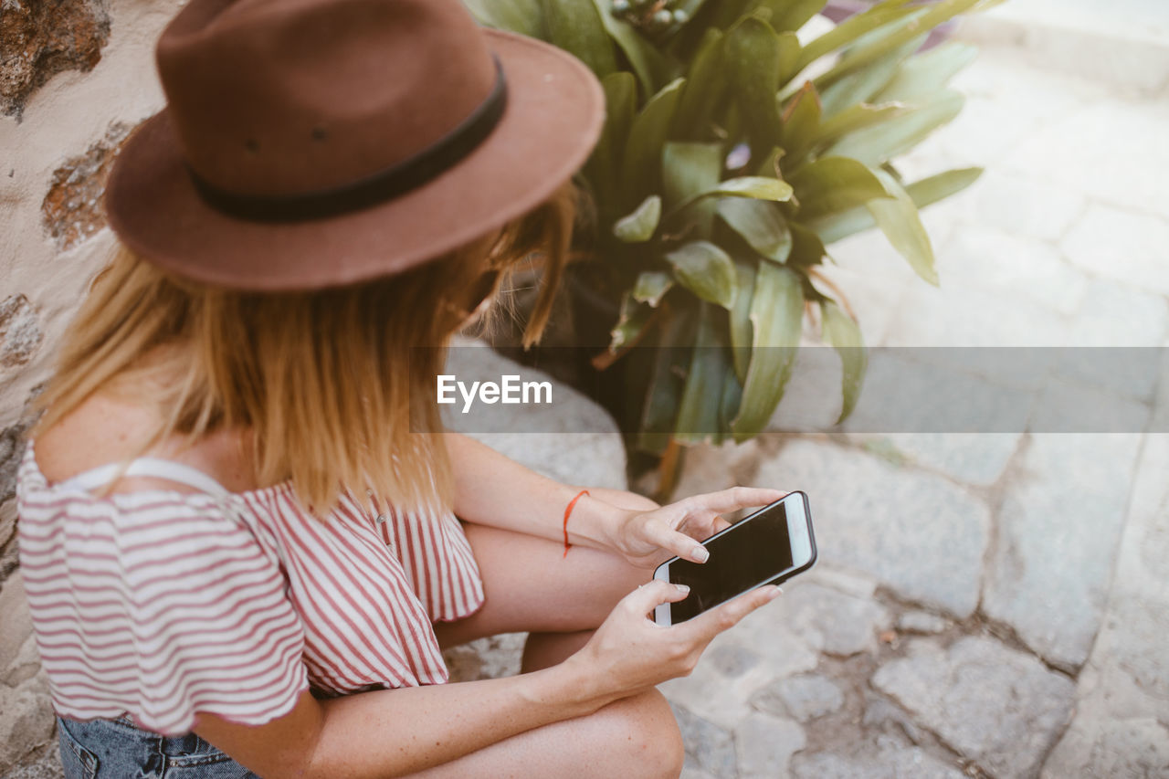 Unrecognizable woman sitting with hat watching her mobile phone