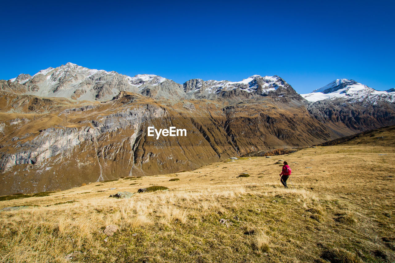 Rear view of woman hiking on mountain against clear blue sky