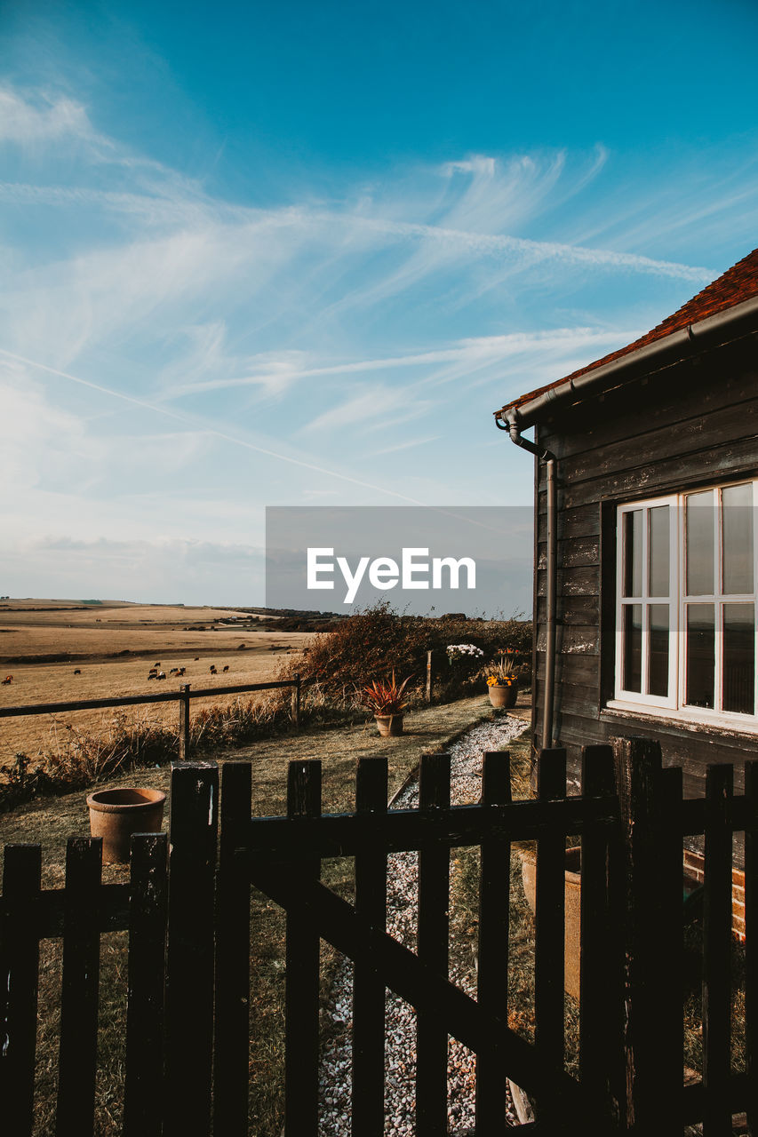 Wooden fence by wooden house against sky near field in english village