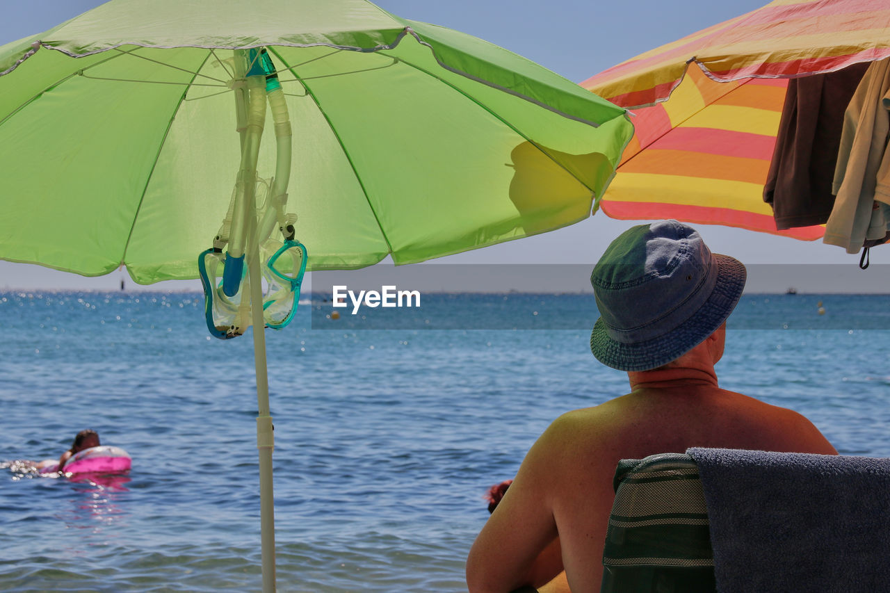 Rear view of man sitting on chair at beach