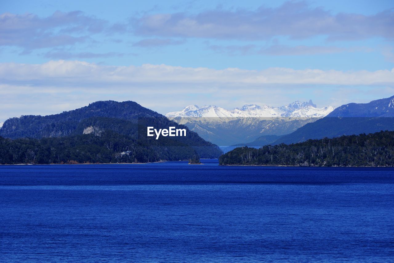 Scenic view of blue river and mountains against cloudy sky