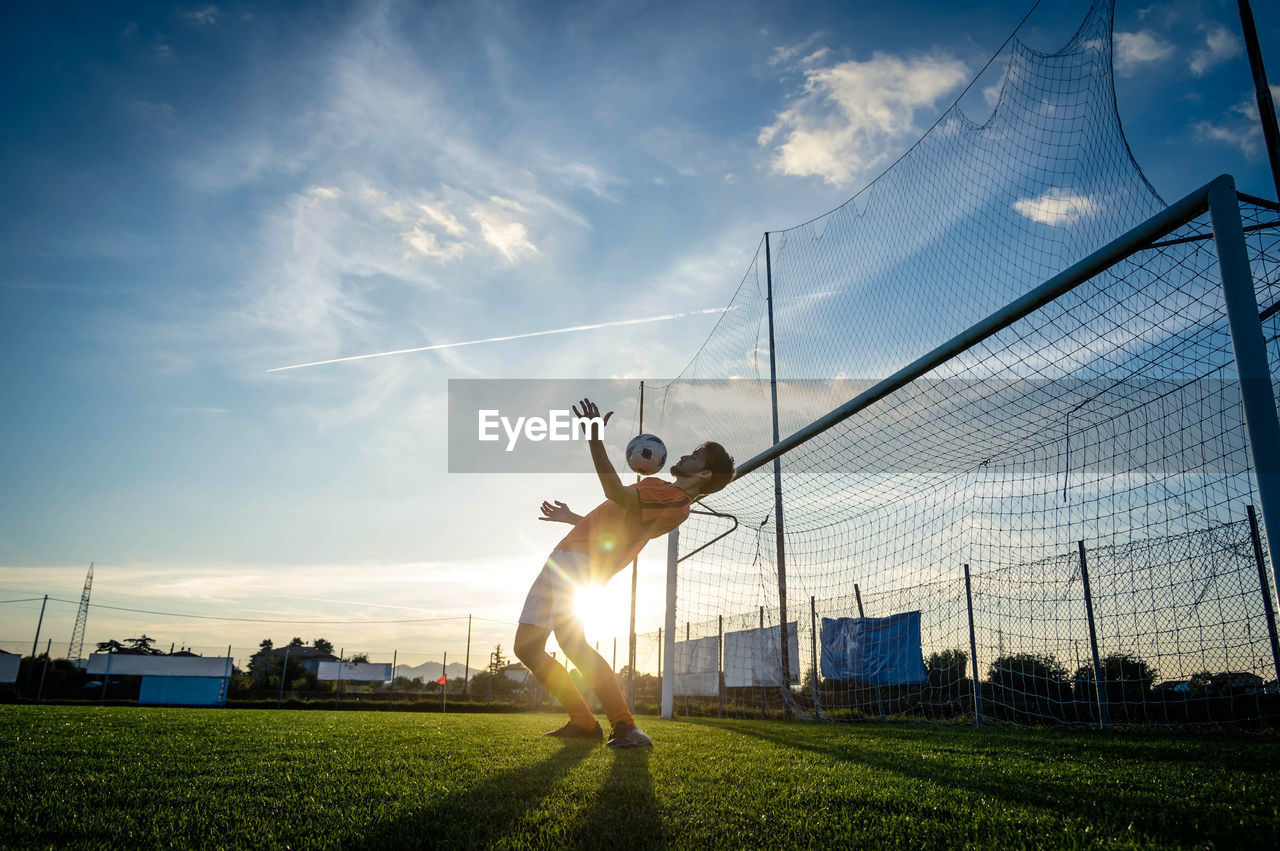 Man playing soccer on field against sky during sunset