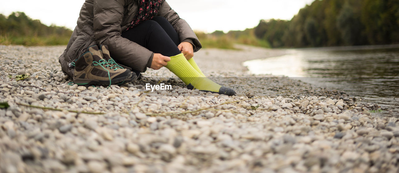 Low section of woman wearing sock at riverbank