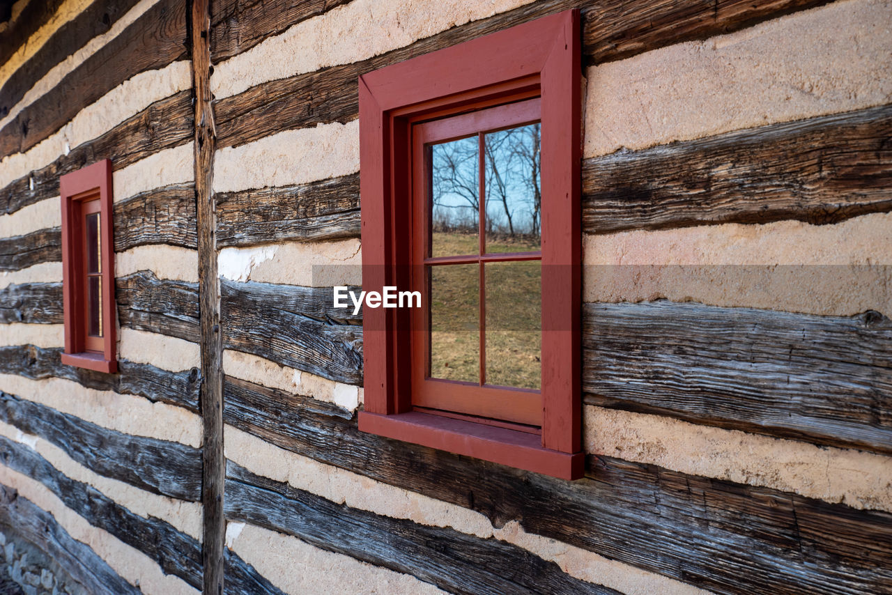 Exterior wall of colonial log cabin with landscape reflected in window