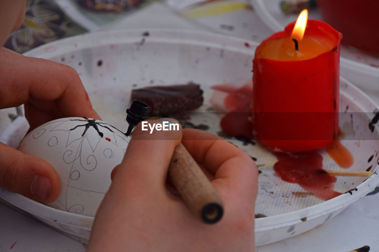 Cropped hand of man wax painting easter egg on table