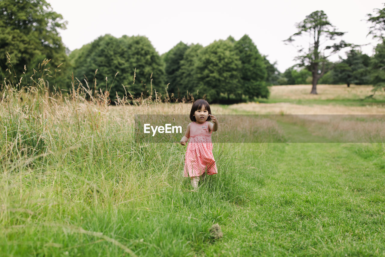 Portrait of girl walking on grass at meadow against sky