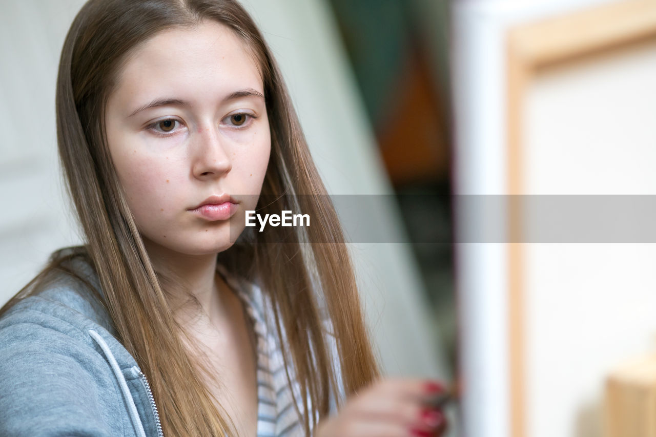 Concentrated young woman painting on canvas