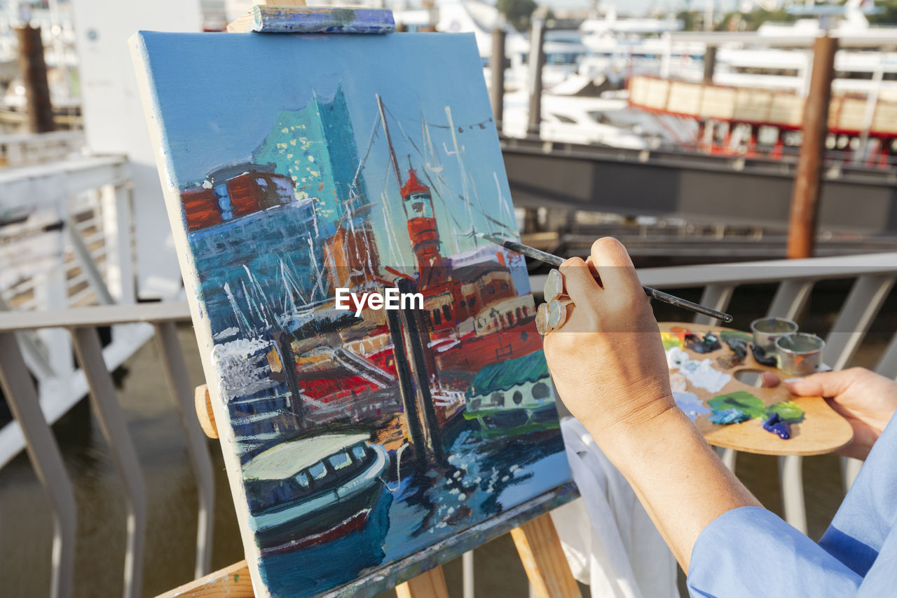Hand of artist painting on easel at harbor