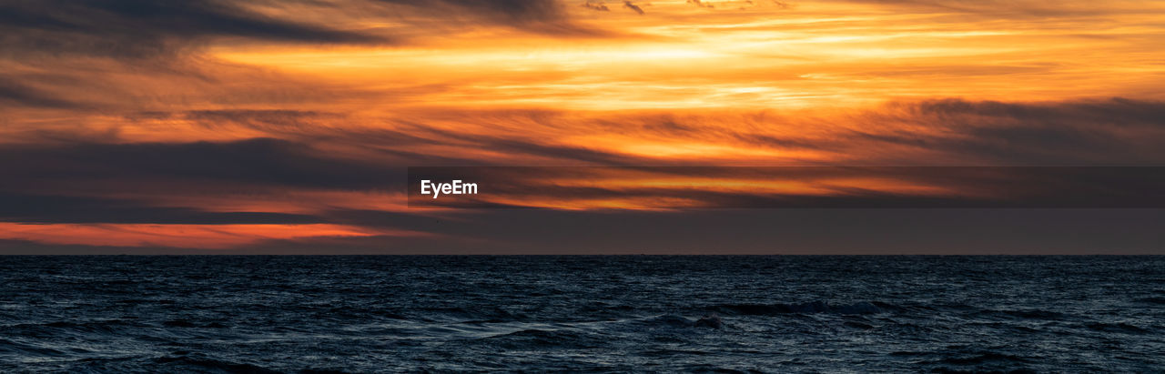 Scenic view of sea against dramatic sky during sunset