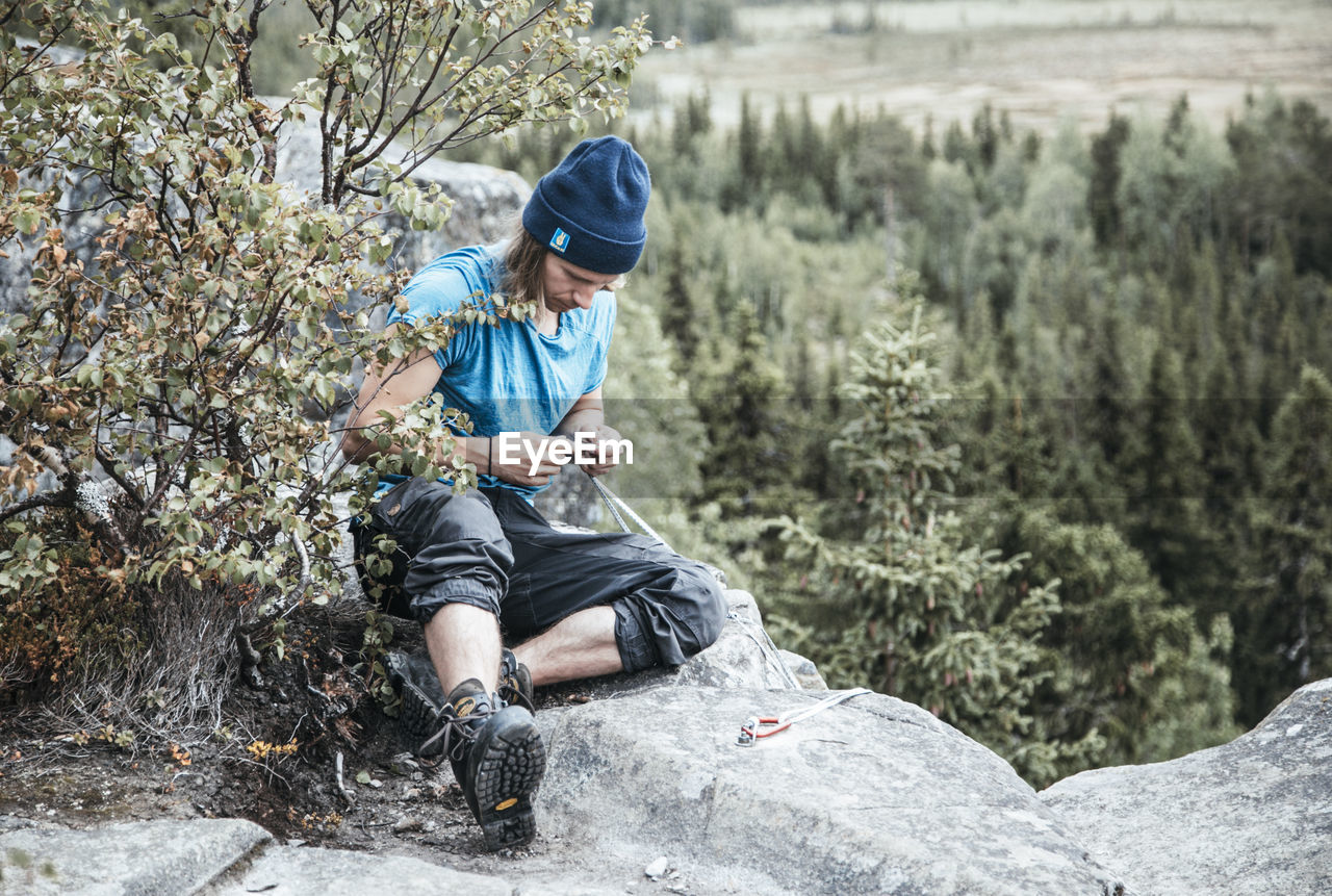 REAR VIEW OF MAN SITTING ON ROCK AT FOREST