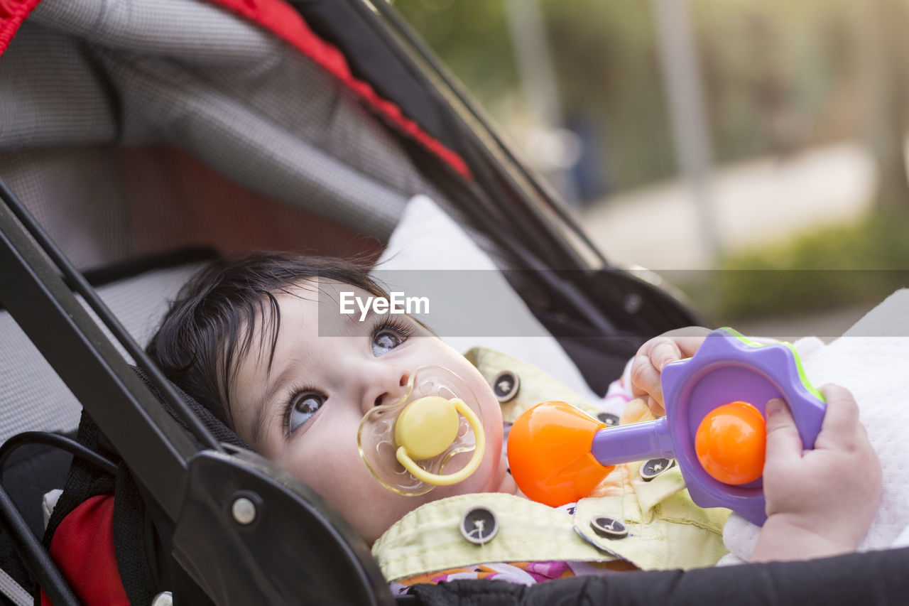 Cute toddler sulking pacifier while looking away in baby stroller outdoors