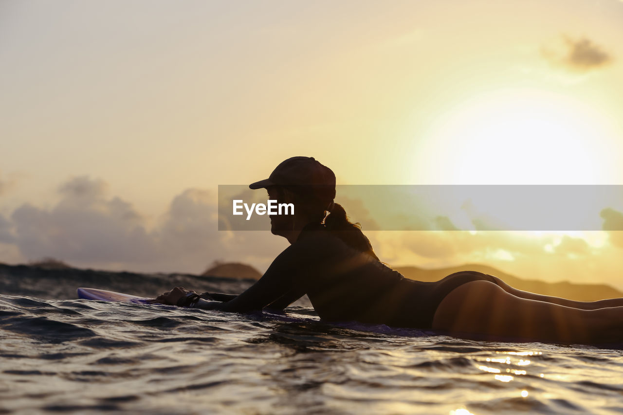 Female surfer lying on surfboard in the evening