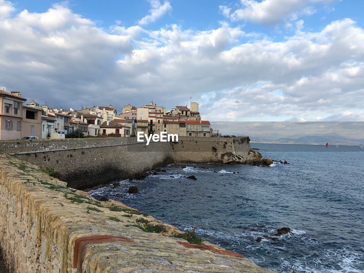 Buildings by sea against cloudy sky