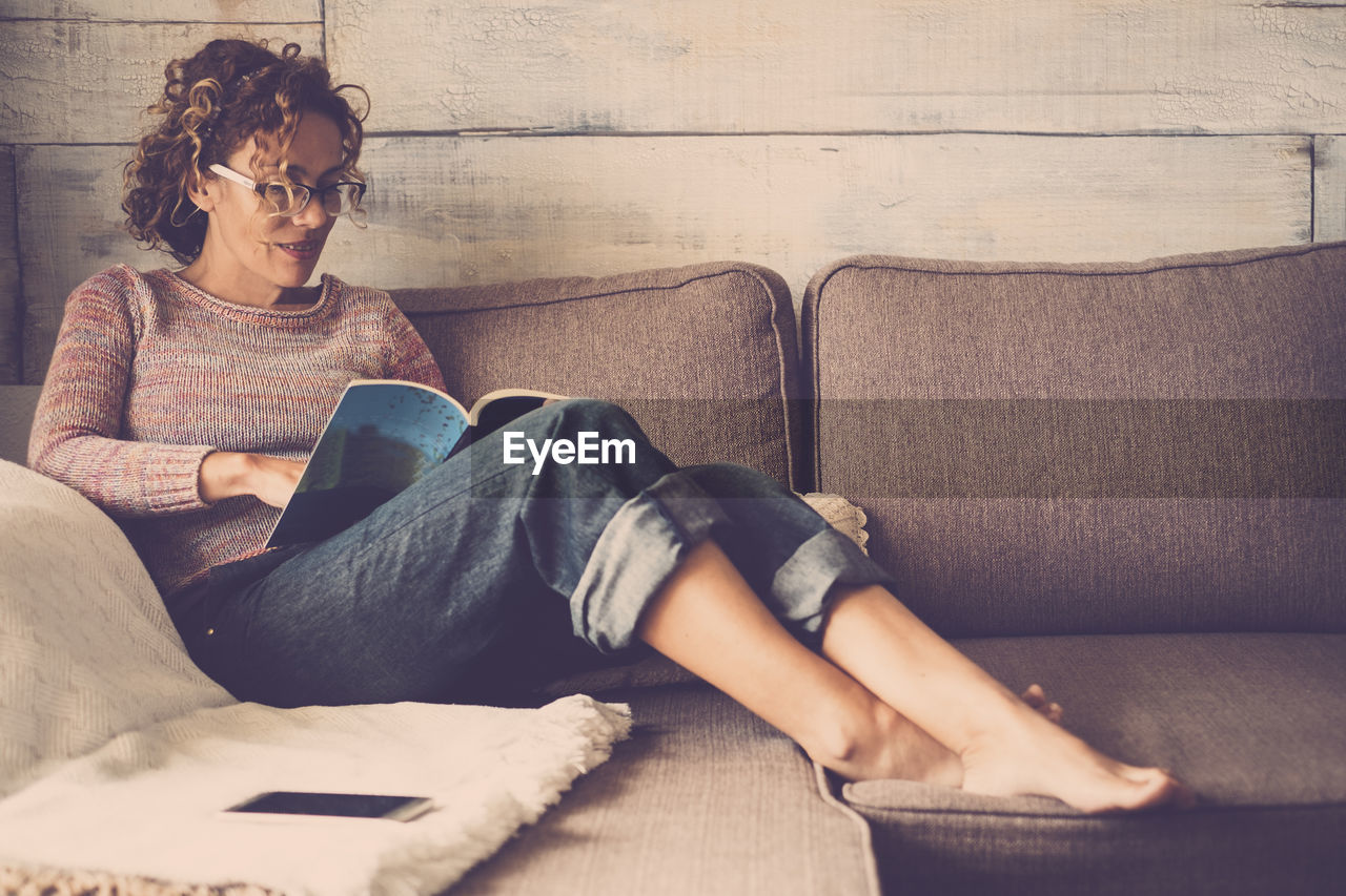 Young woman reading book while relaxing on sofa at home