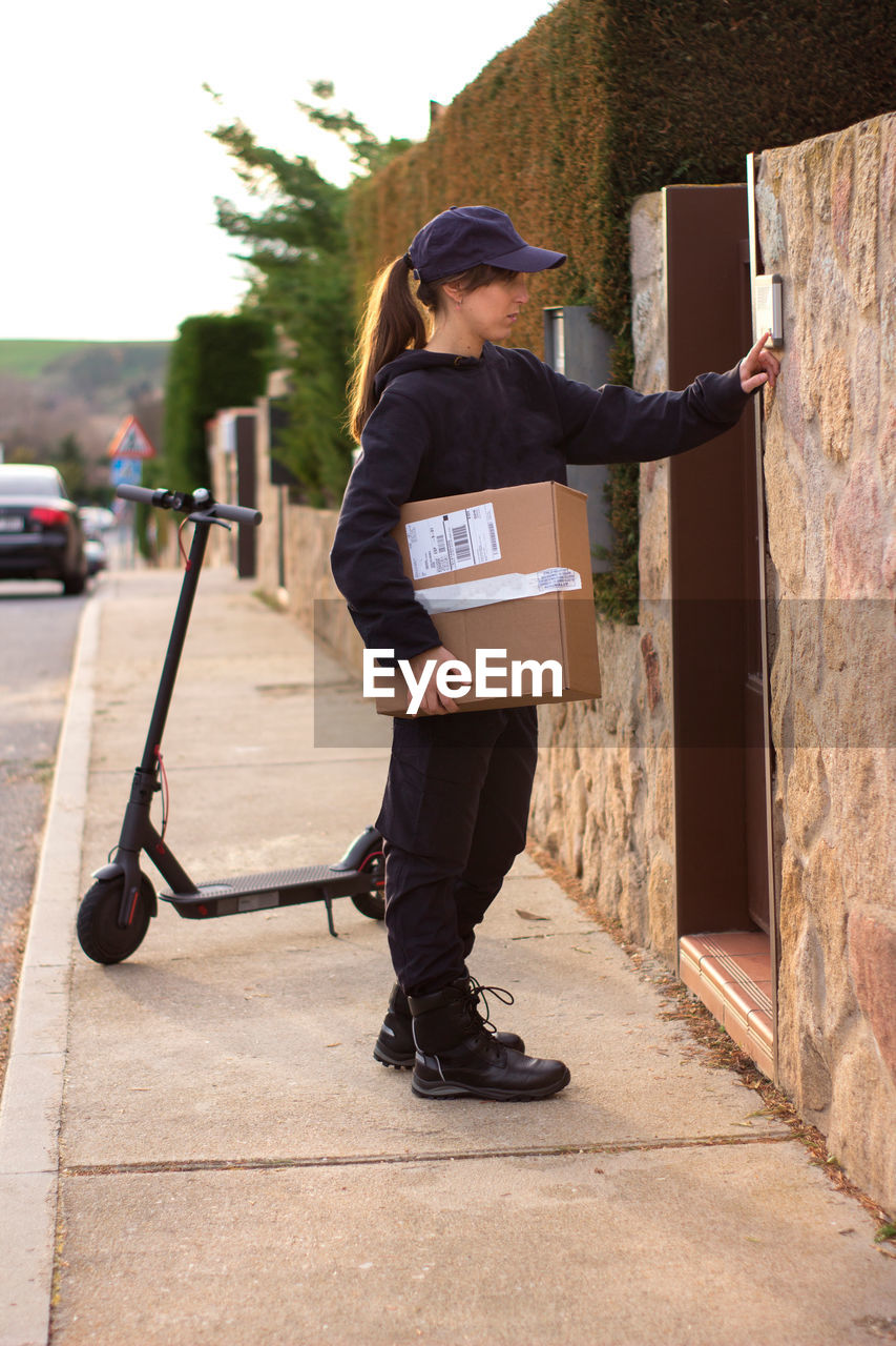 Full length of delivery person holding parcel standing on footpath