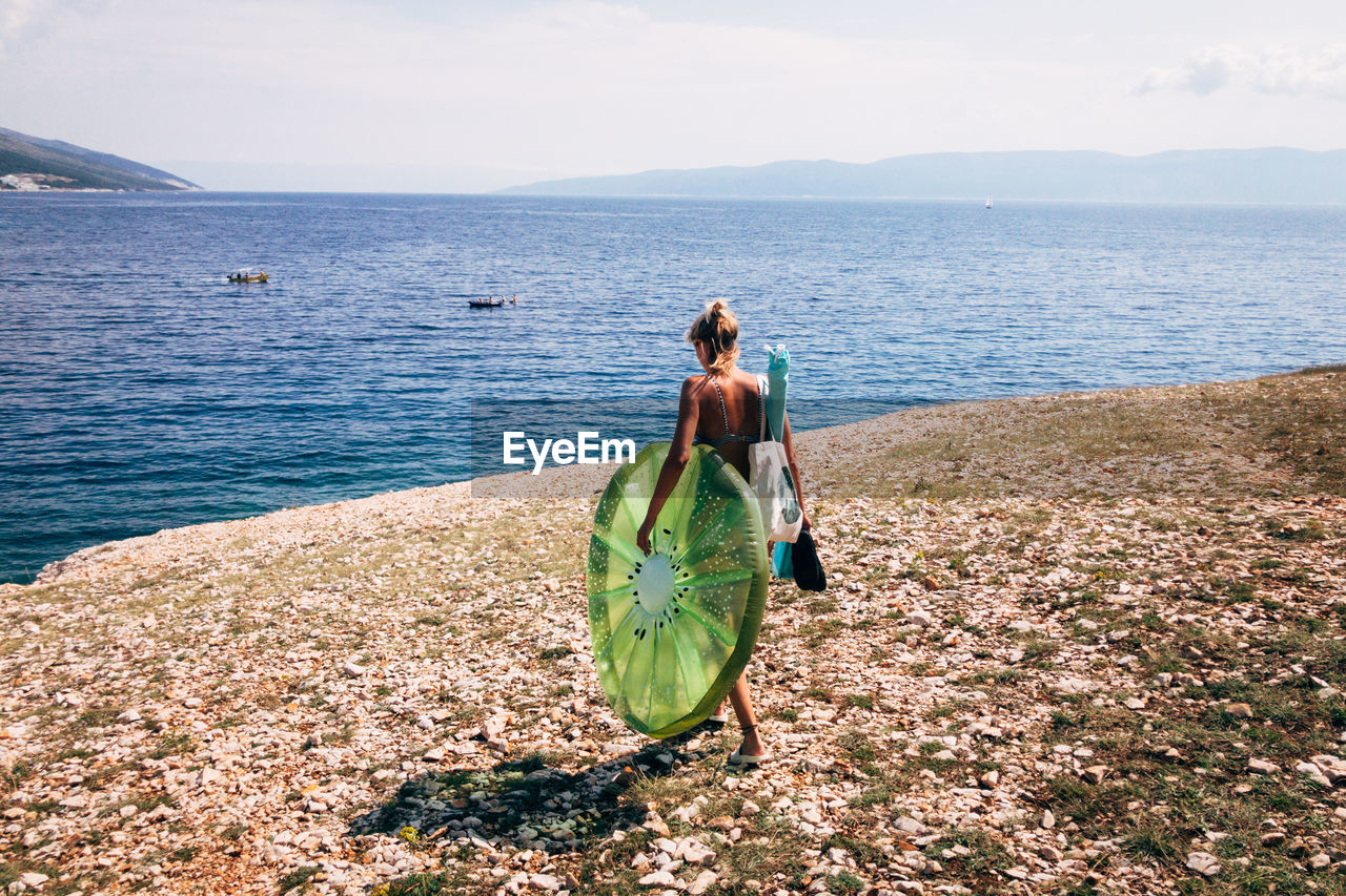 Rear view of woman with pool raft walking at beach