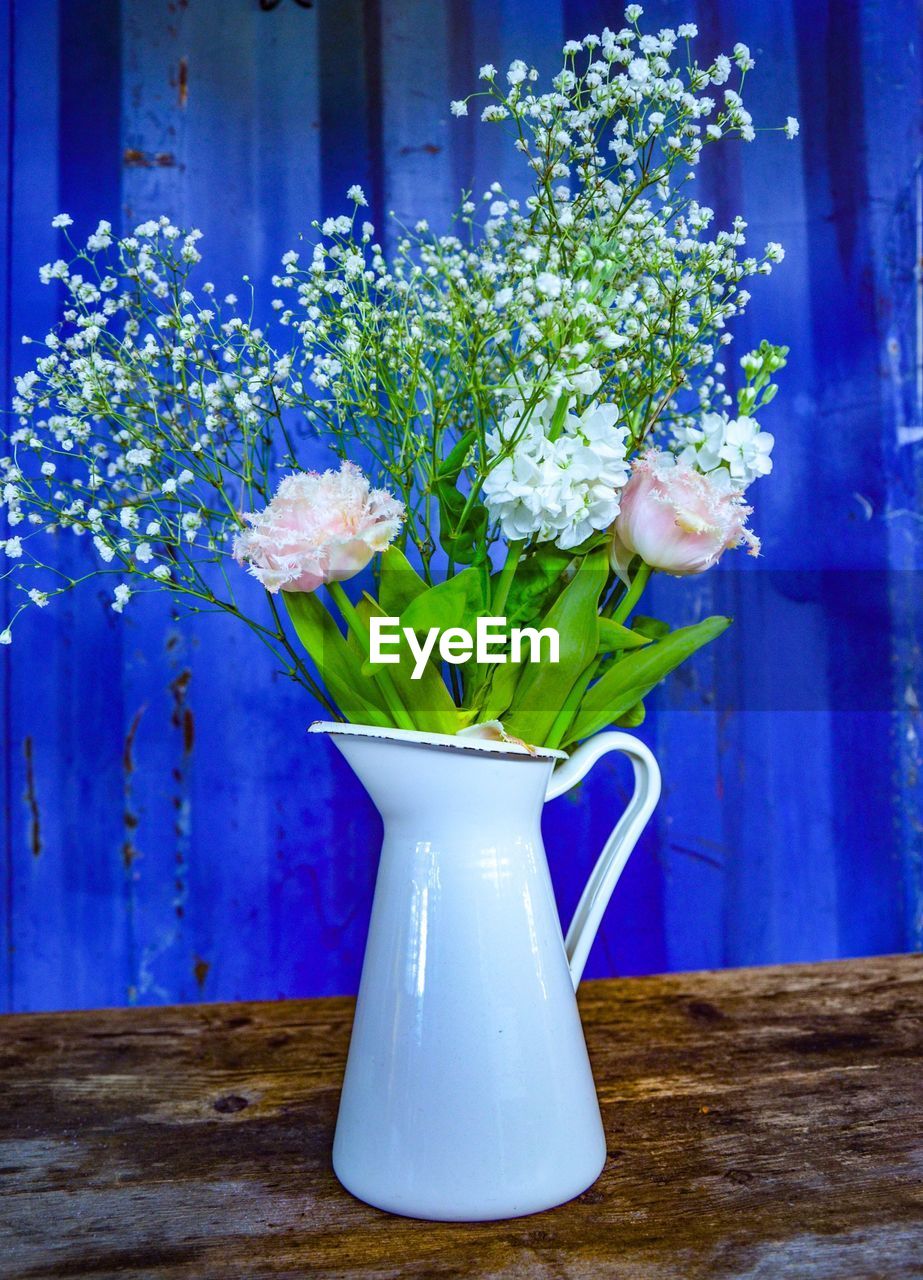 Close-up of flower vase on table in front of blue metal wall