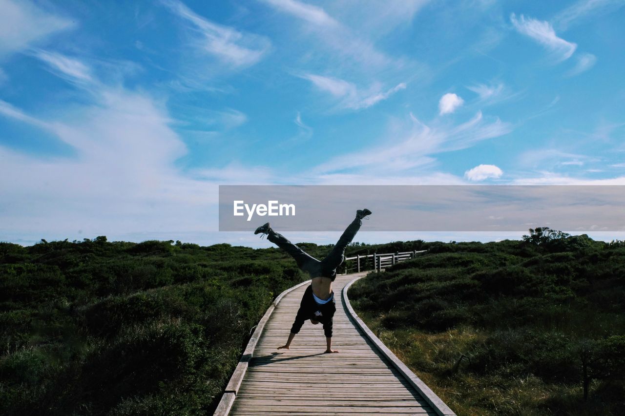 Full length of man using handstand on boardwalk against sky