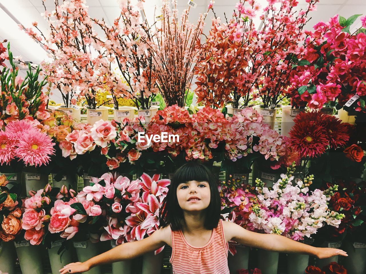 Portrait of girl with arms outstretched standing against pink flowers