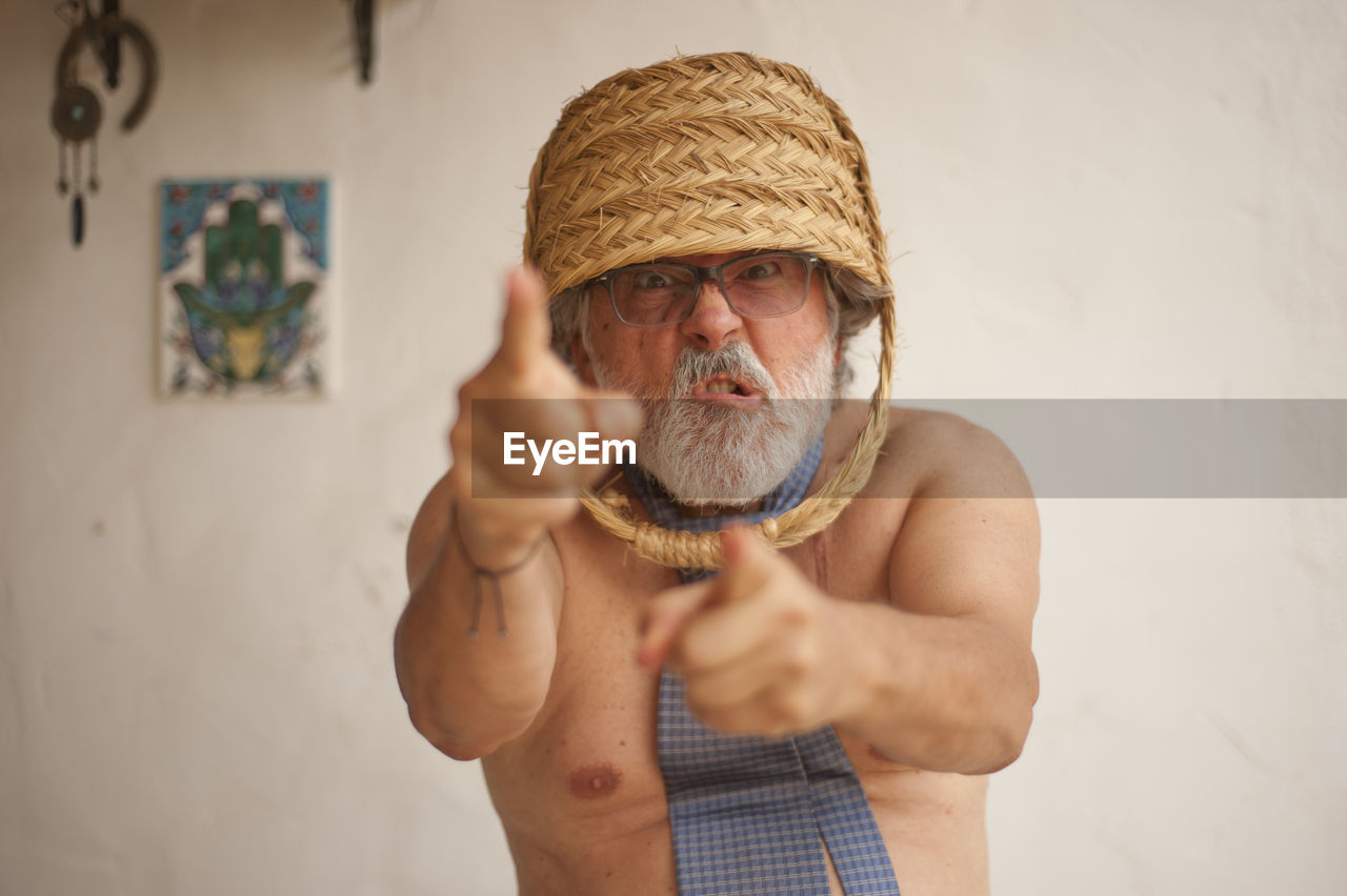 Portrait of angry man wearing basket on head while standing against wall