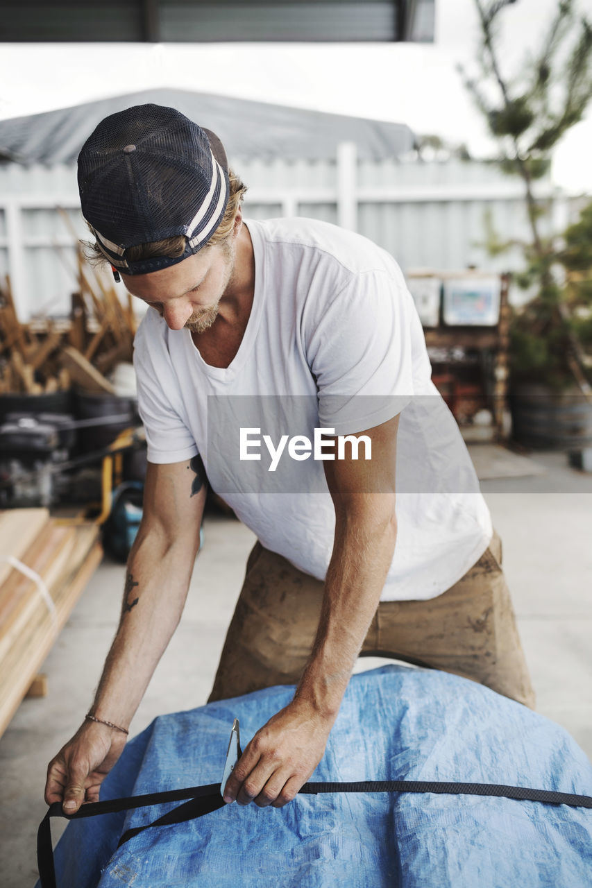 Male carpenter fastening belt to package at workshop