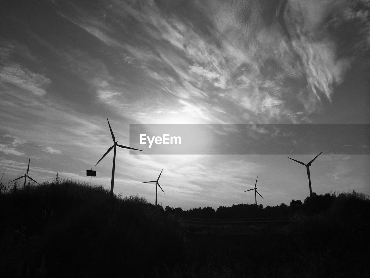 Wind turbines on field against cloudy sky