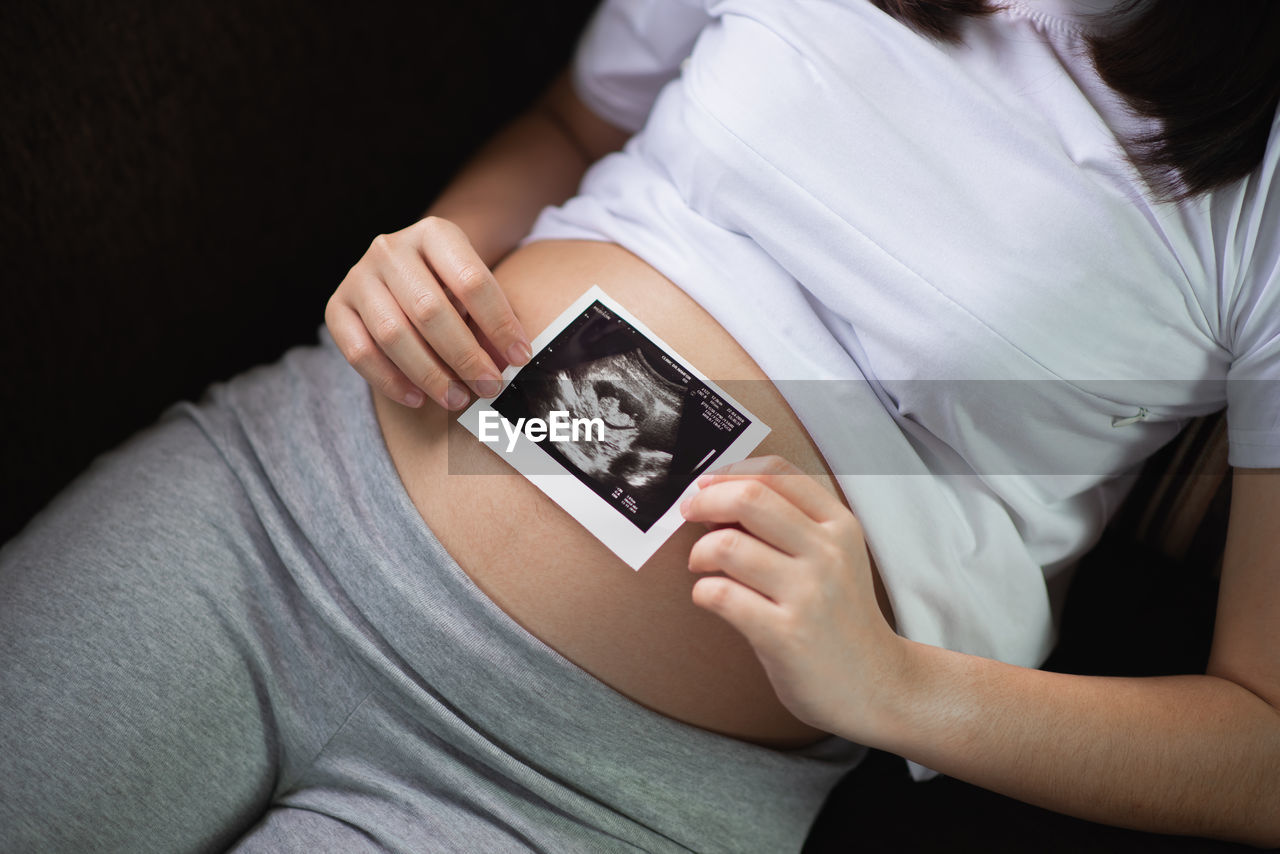 Midsection of pregnant woman holding x ray at home