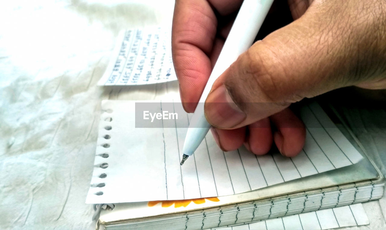 CLOSE-UP OF HAND HOLDING BOOK WITH PAPER