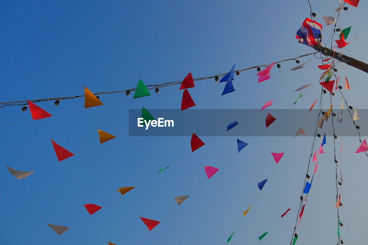 Low angle view of bunting hanging against clear blue sky