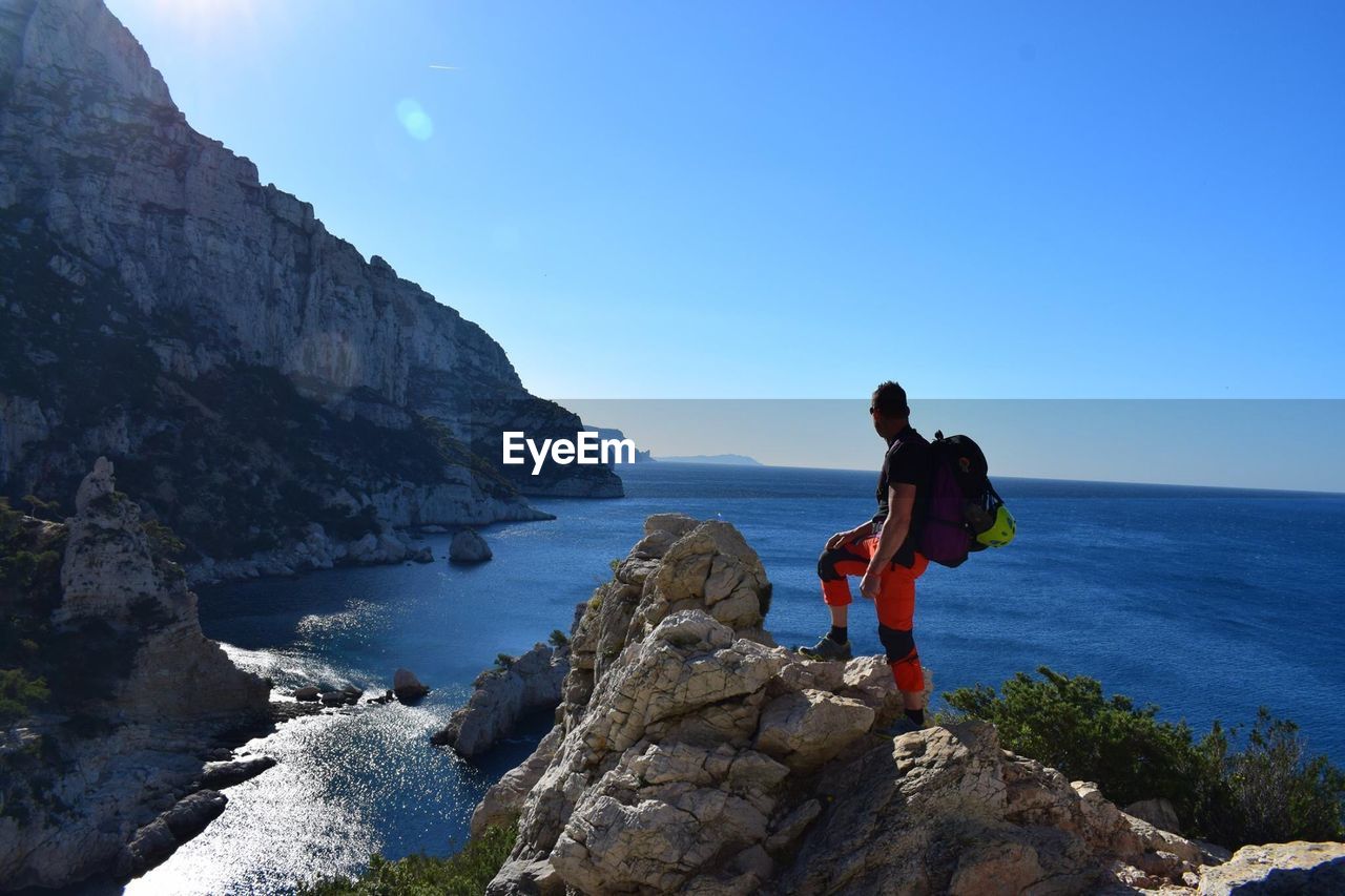 Side view of male hiker standing on cliff against sea