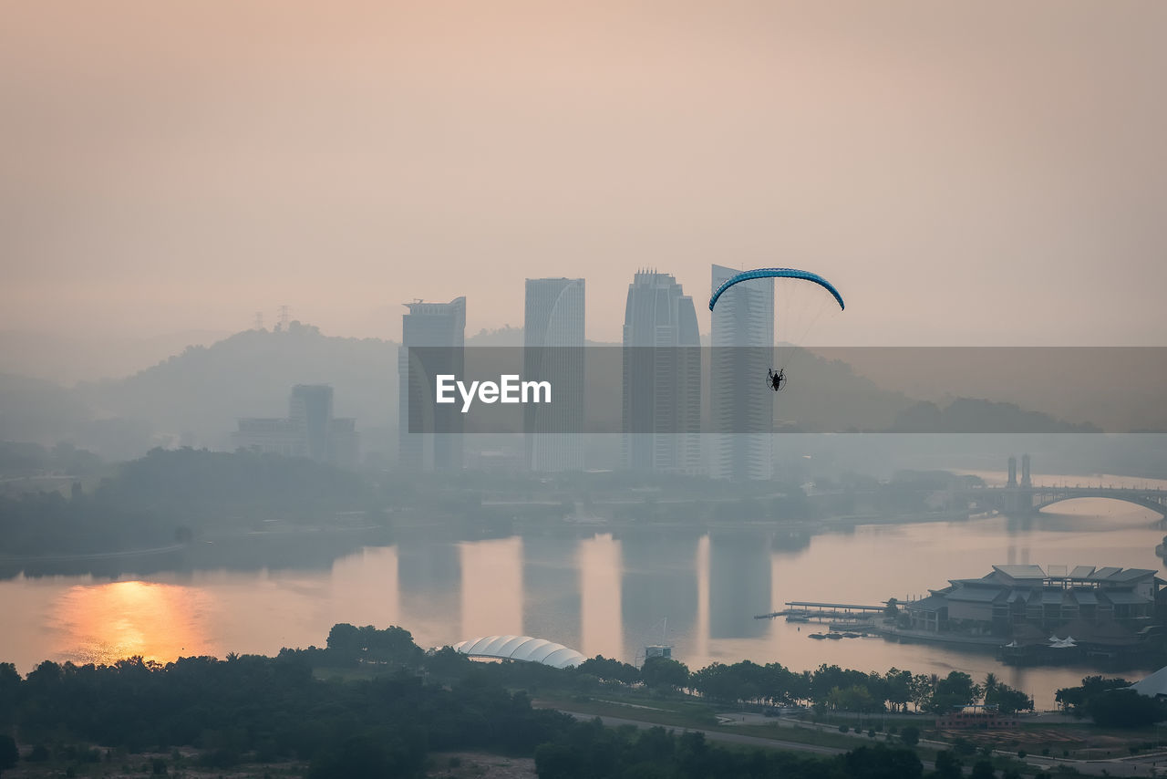 Parachute flying above river in foggy weather during sunrise