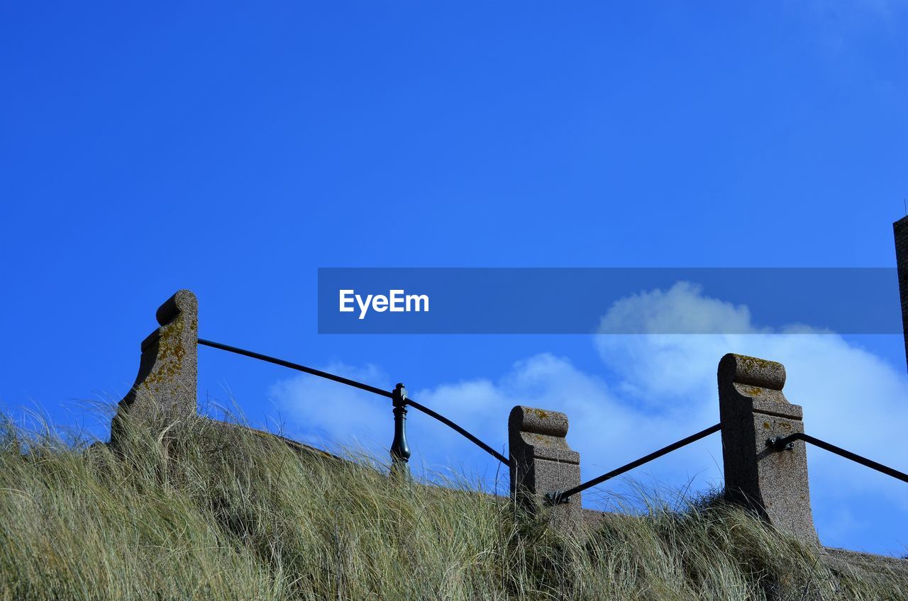 Low angle view of fence on field against blue sky