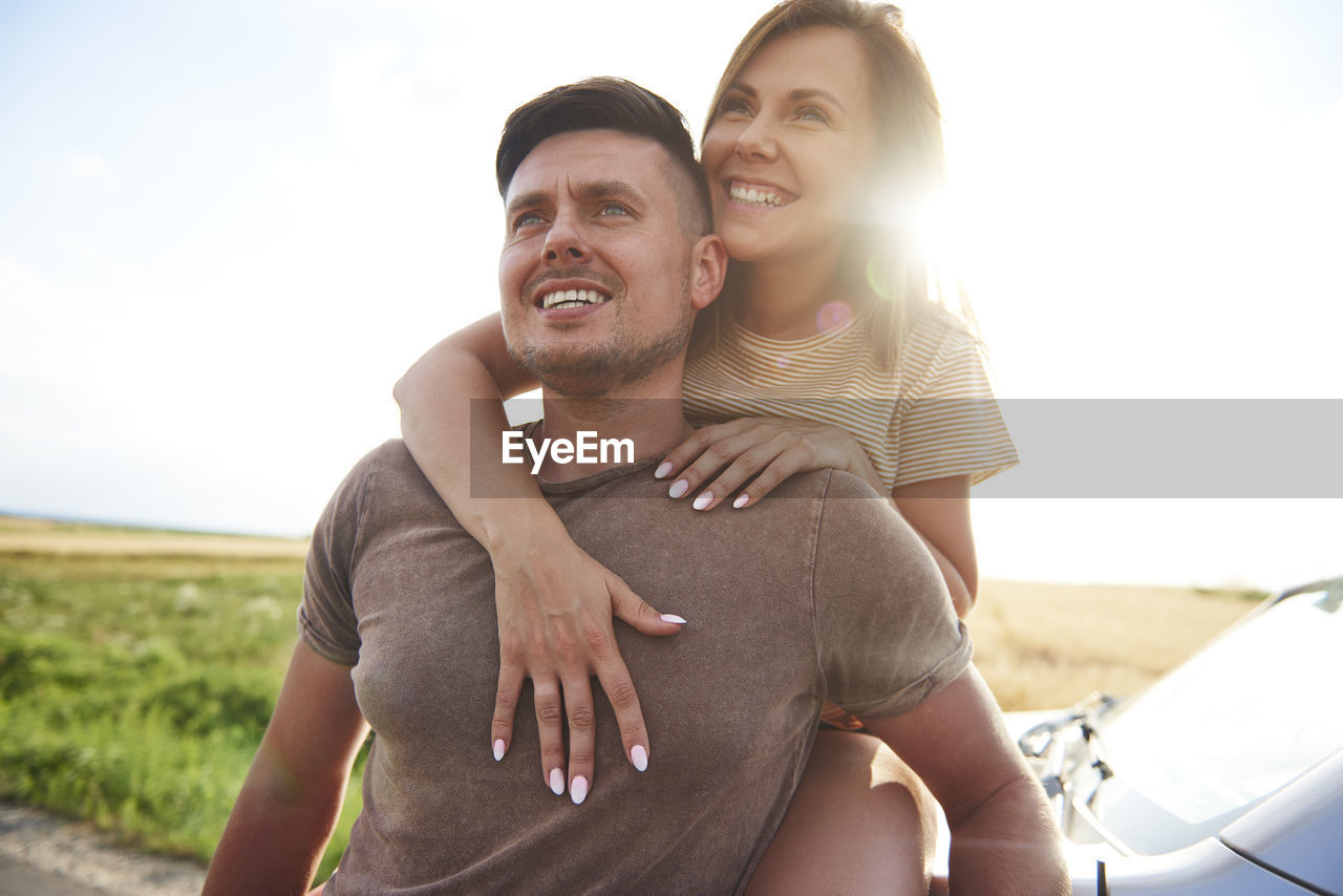 Smiling couple by car against clear sky