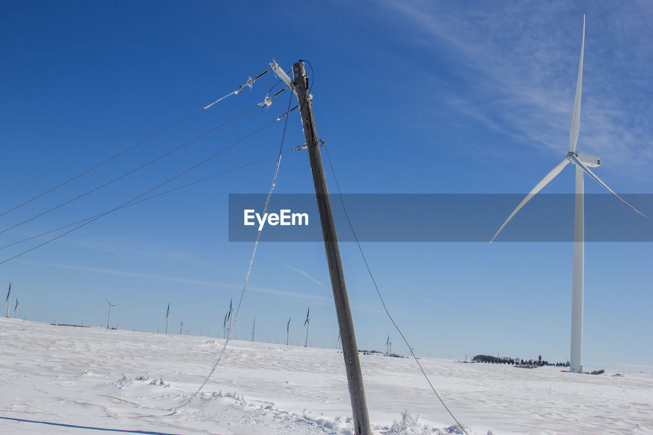 Leaning power pole with wind turbines in the background.