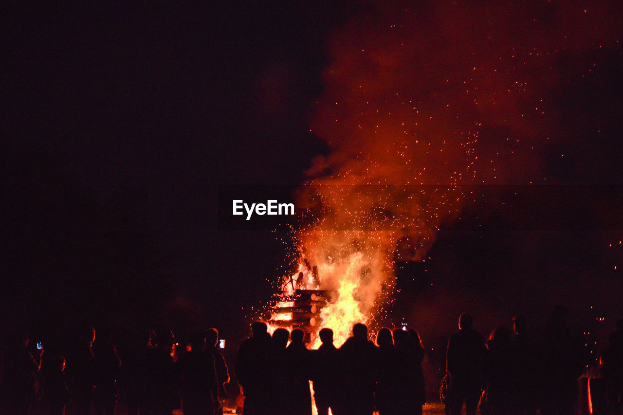 Silhouette people enjoying bonfire on field at night