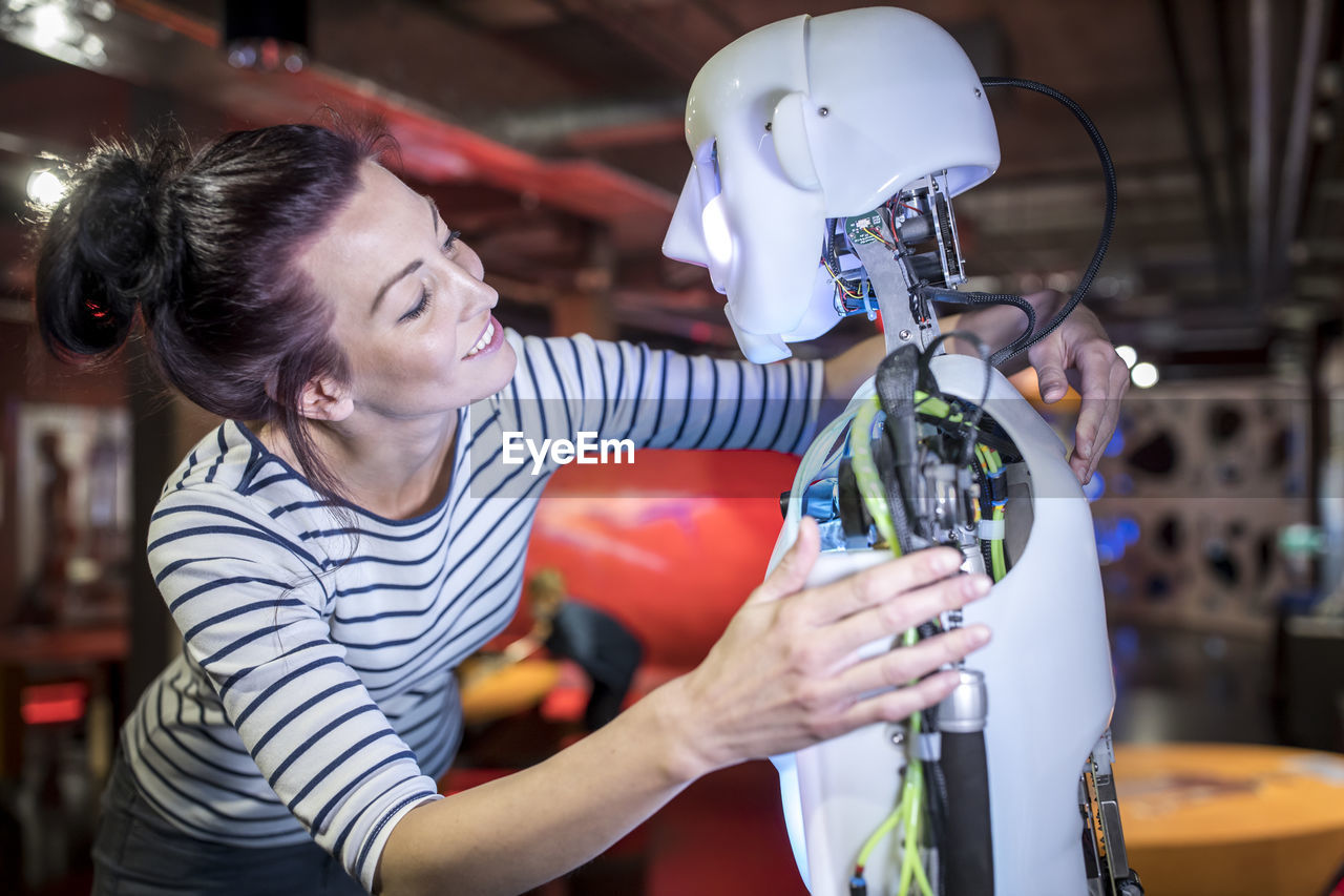 Smiling technician with arm around human robot at workshop