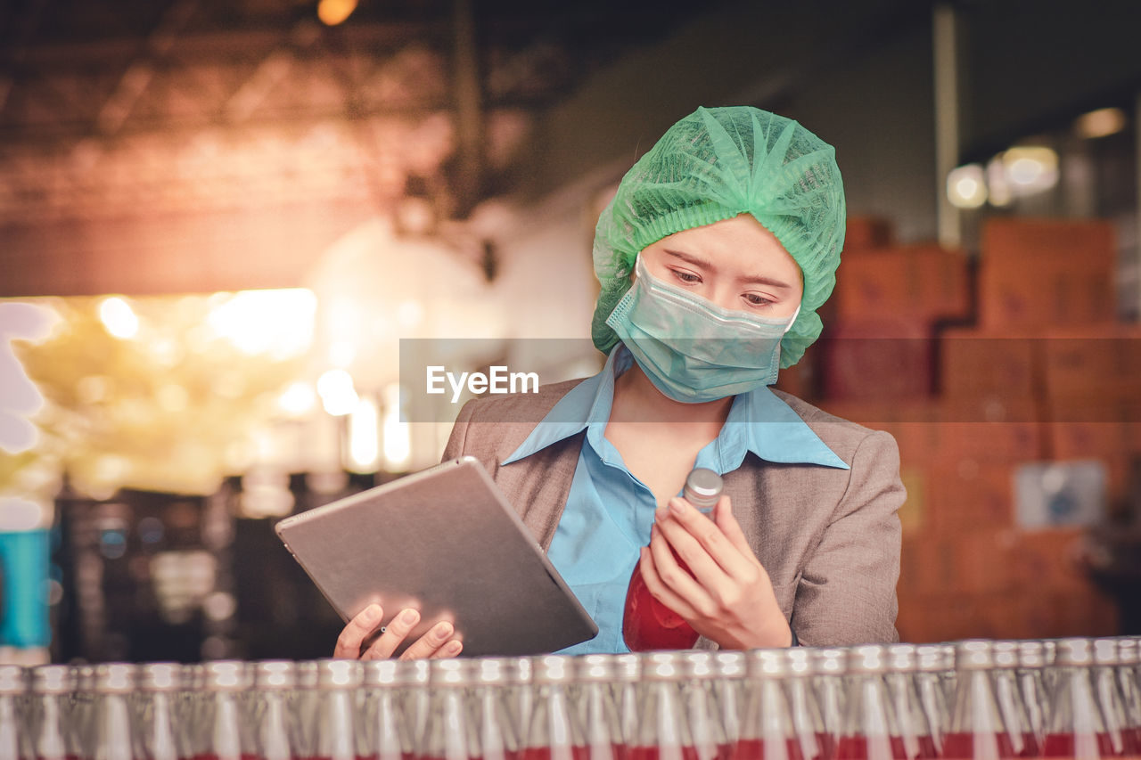 Woman using digital tablet while inspecting drinks in factory