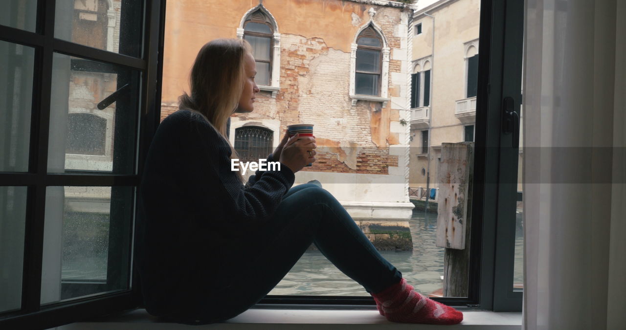 SIDE VIEW OF WOMAN SITTING IN WINDOW