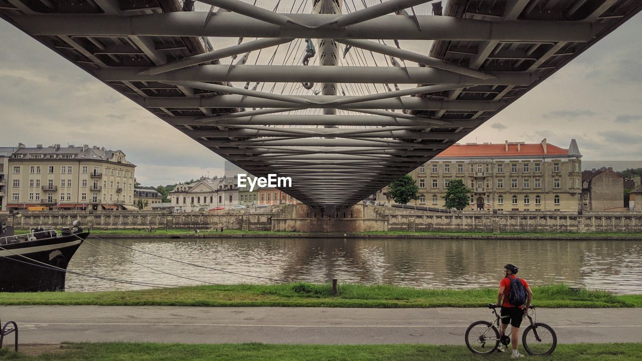 MAN RIDING BICYCLE ON BRIDGE OVER RIVER