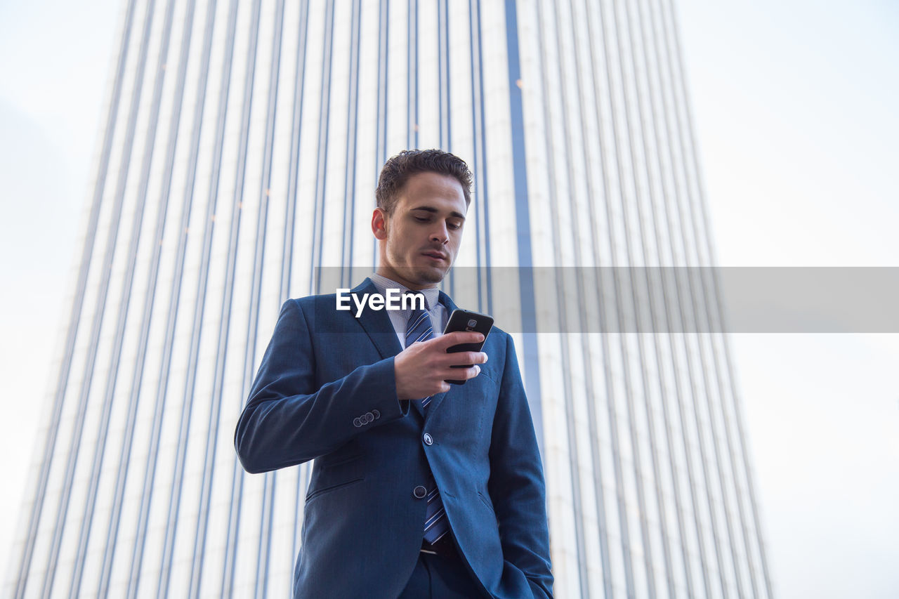 Low angle view of businessman using phone against wall
