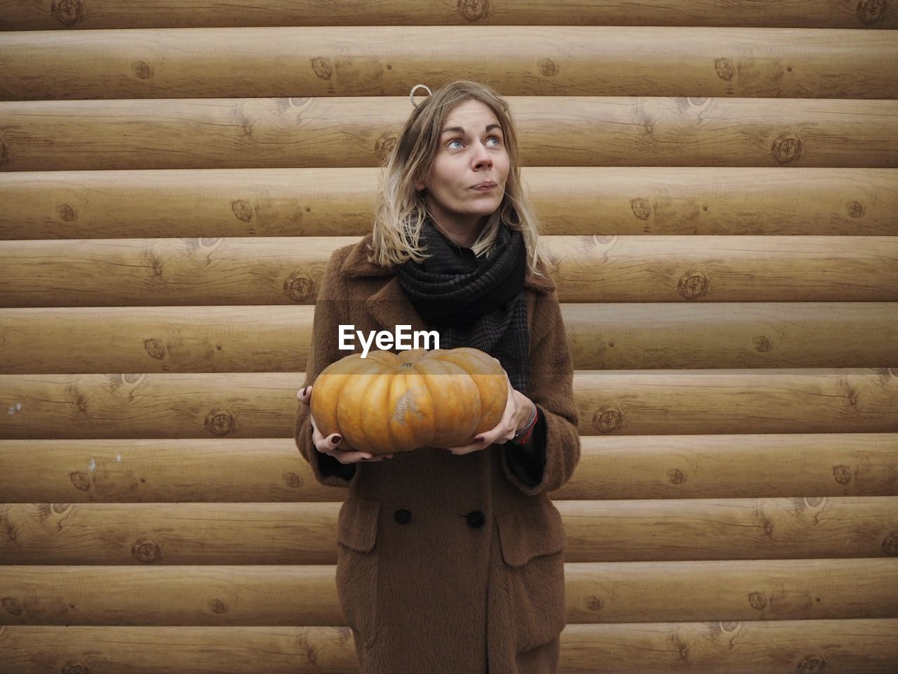 Woman holding pumpkin while standing by wooden wall
