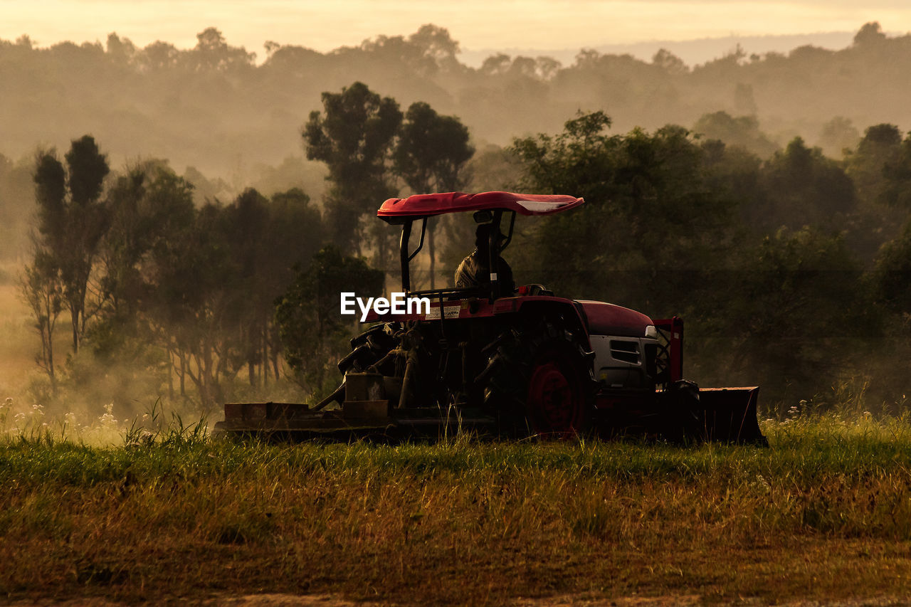 TRACTOR ON FIELD AGAINST TREES AND SKY