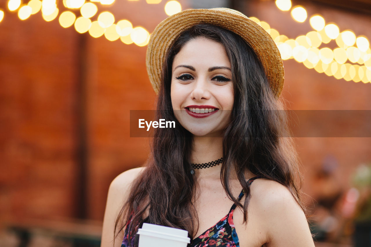 PORTRAIT OF SMILING YOUNG WOMAN AGAINST BLURRED BACKGROUND