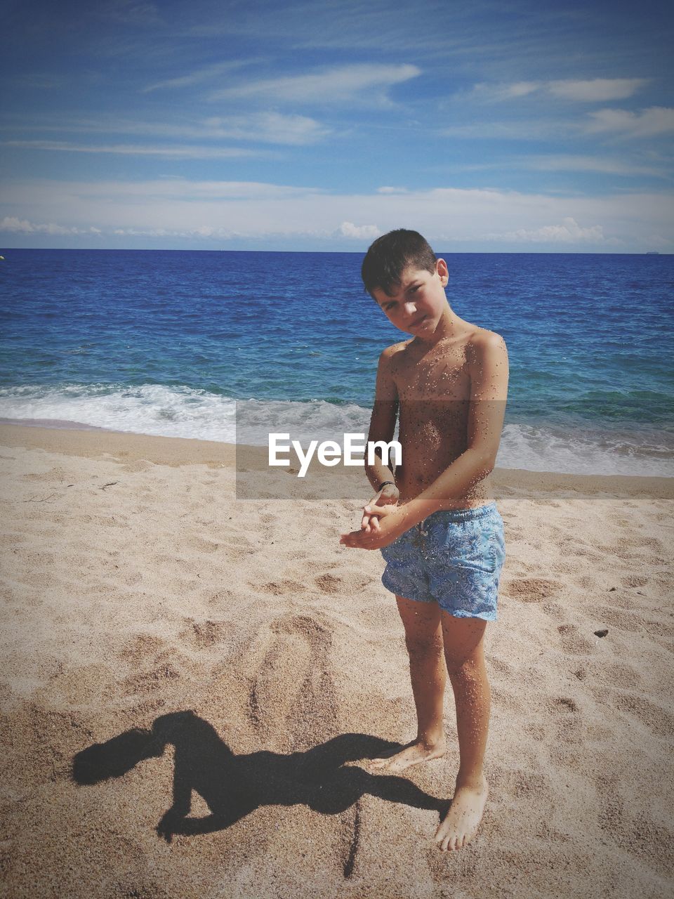Portrait of shirtless boy standing at beach against sky