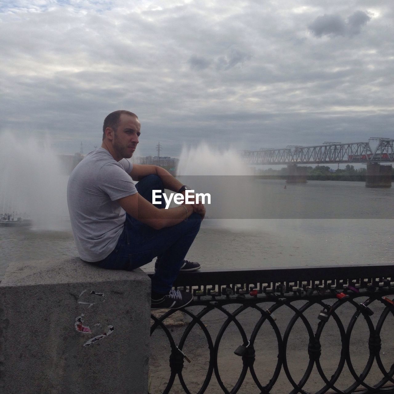 Young man sitting against river during sunset