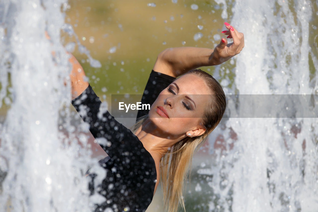 Beautiful woman with hand raised standing against fountain