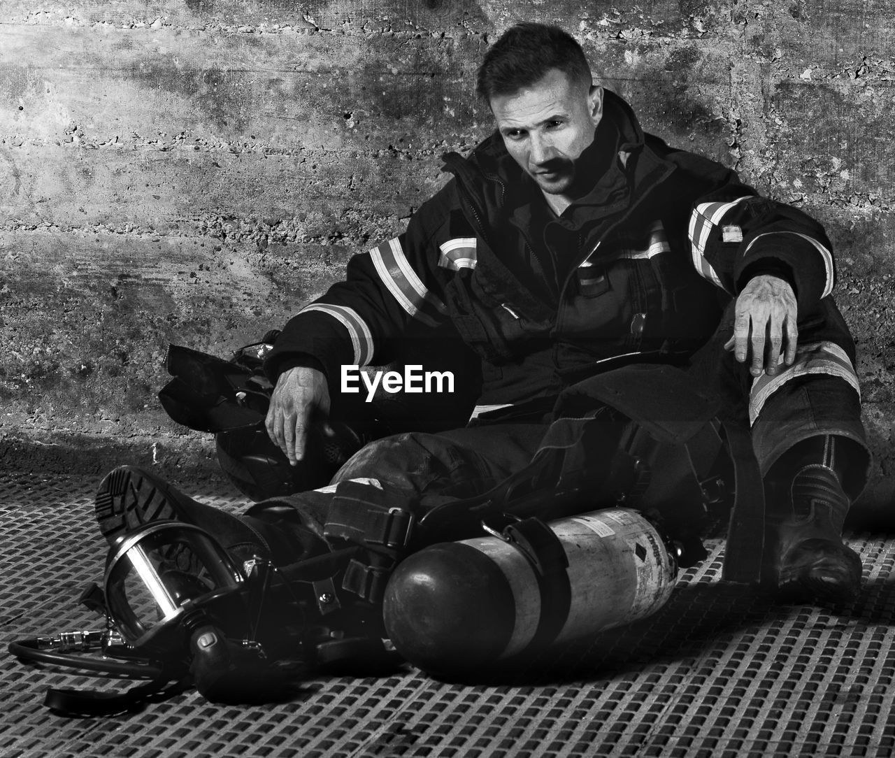 Full length of firefighter sitting against wall