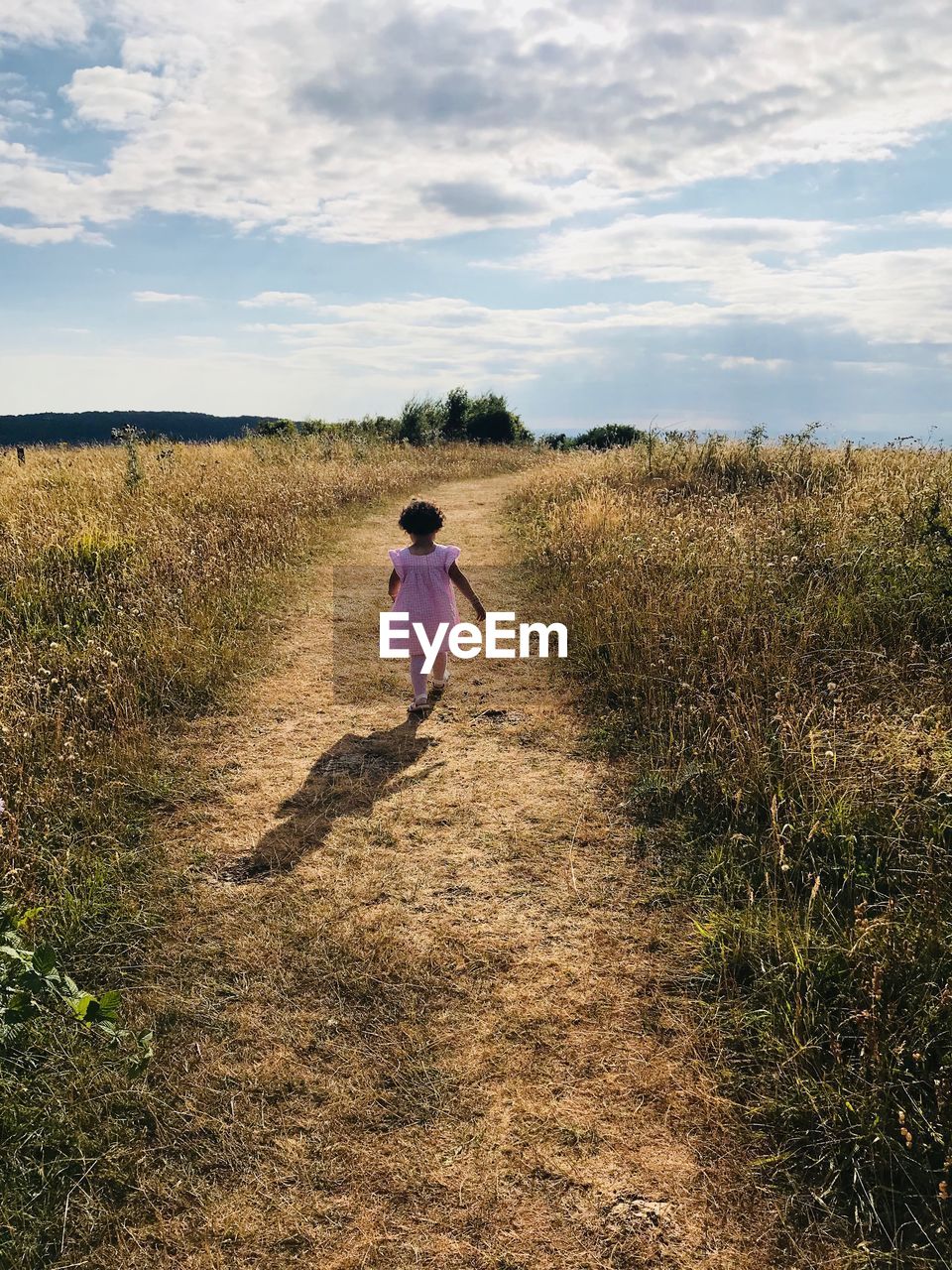 Rear view of girl walking on field against sky