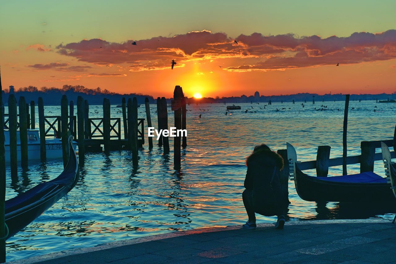 Silhouette men crouching on pier by sea against sky during sunset